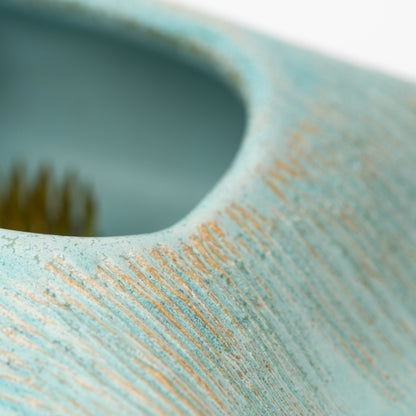 Close-up of combed lines beside the pale blue vase opening.