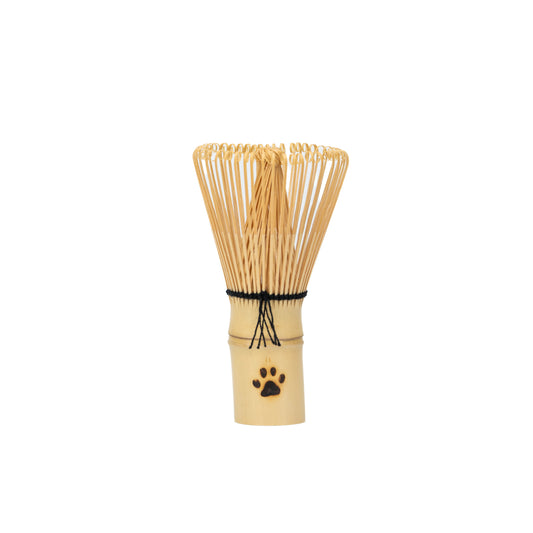 Small bamboo matcha whisk with curled tines, black binding and a paw-print handle on white.