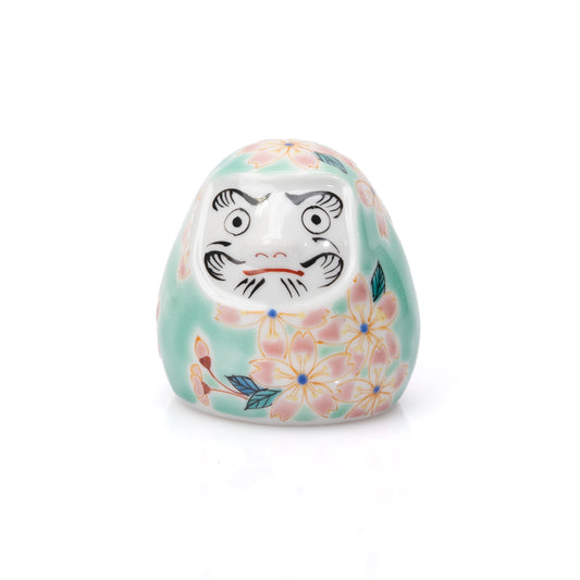 Pale turquoise Kutani daruma with pink cherry blossoms and a white face on white.