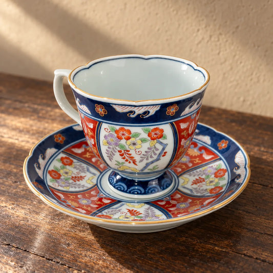 Sehyo Kiln Ko-Imari wisteria cup resting empty on its richly painted saucer on a dark wood table.