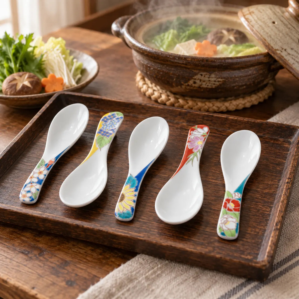 Five Seikō Kutani floral porcelain soup spoons on a wooden tray beside a hot pot