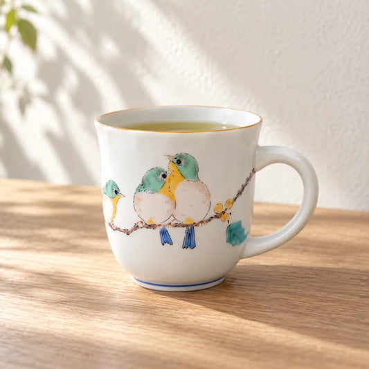 Seikou Kutani mug with three painted mejiro birds, filled with tea on a sunlit wooden table.