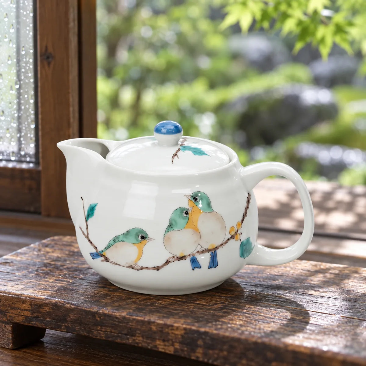 Seikou Kutani teapot with three painted mejiro birds beside a garden window