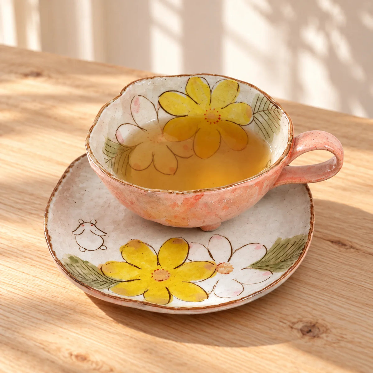 Tasse tripode Seto à lapin et motifs floraux, contenant du thé sur sa soucoupe assortie, laissant visibles le petit lapin et les fleurs peints à la main