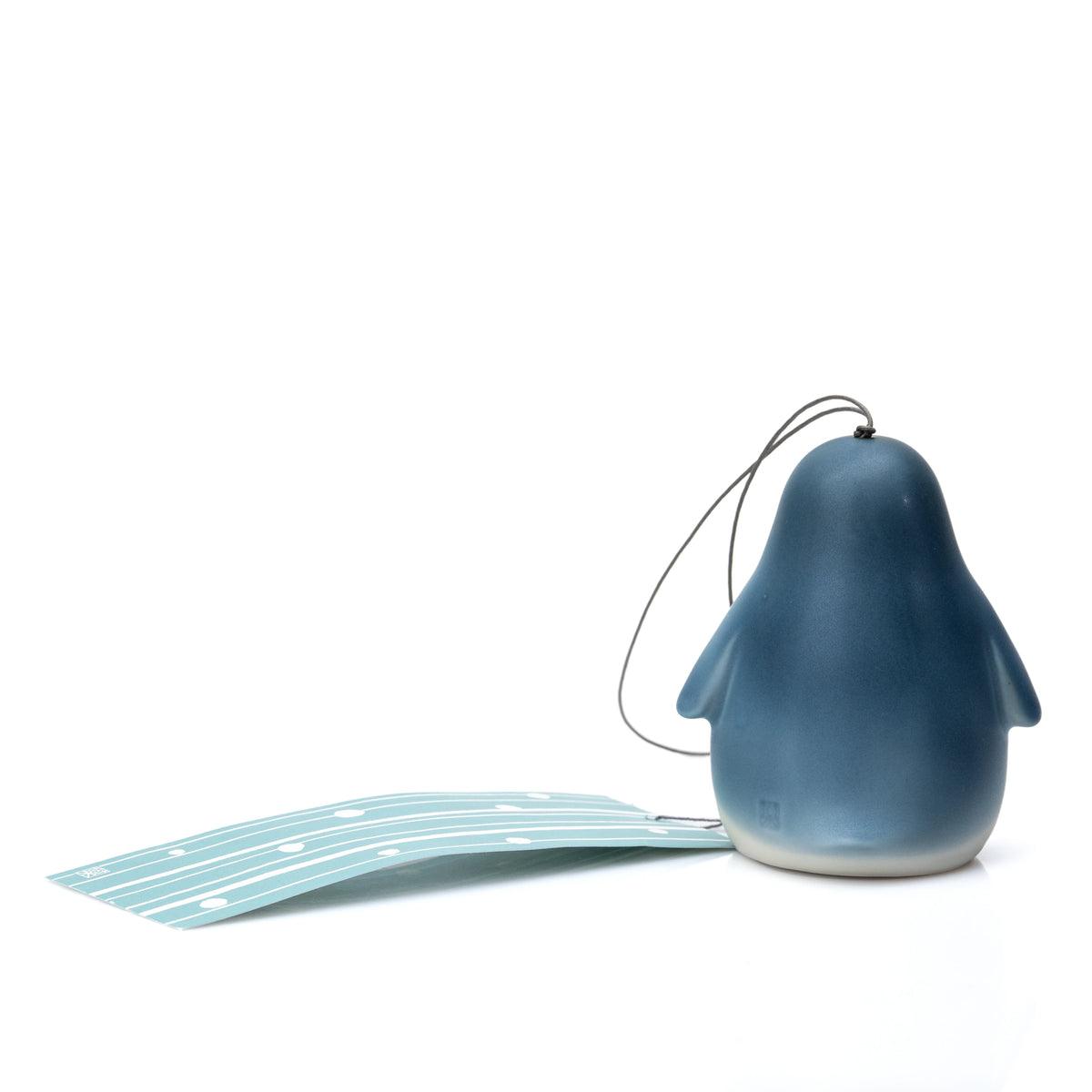 Back of the blue and white penguin wind chime beside its paper strip.