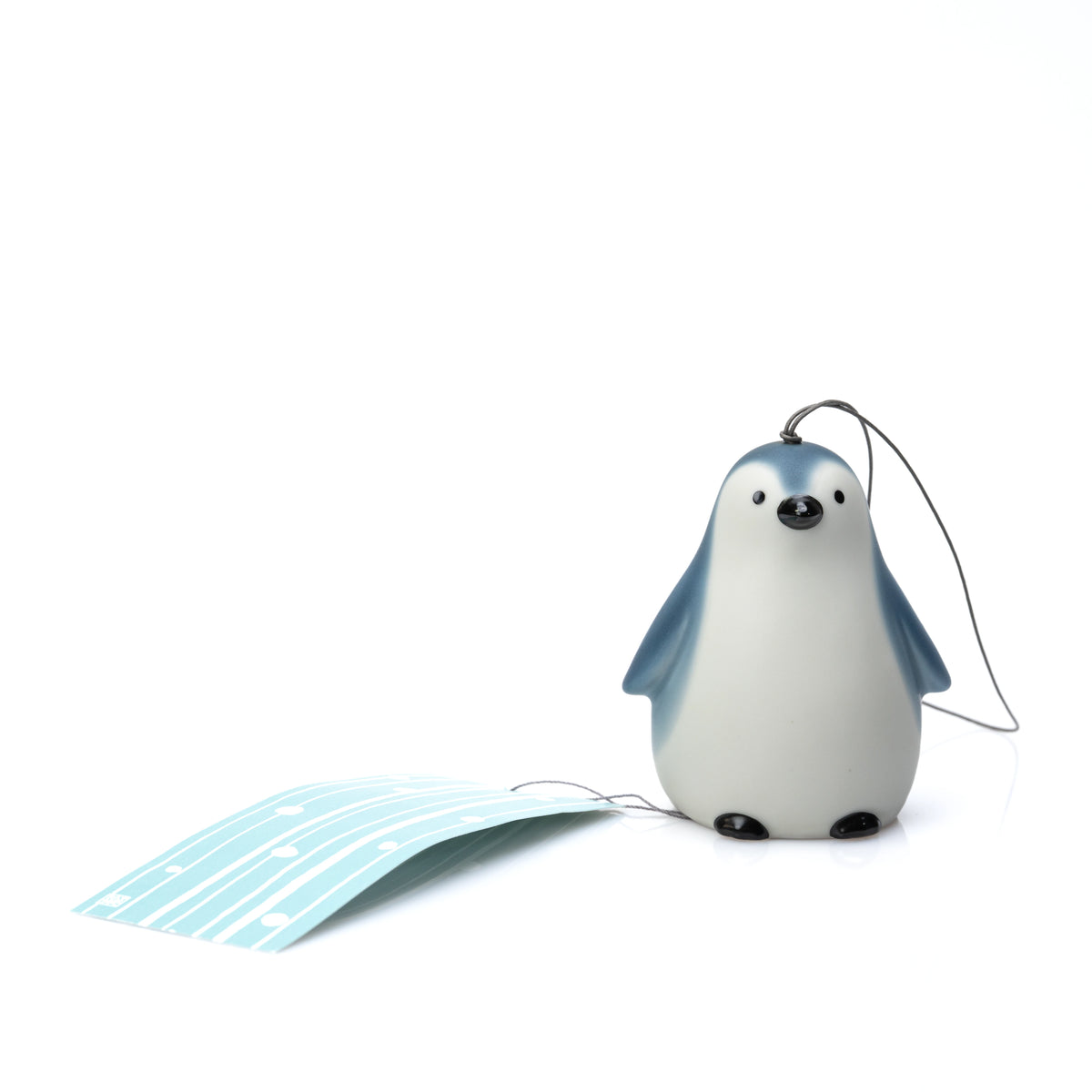 Penguin wind chime resting on a white surface with its paper strip extended.