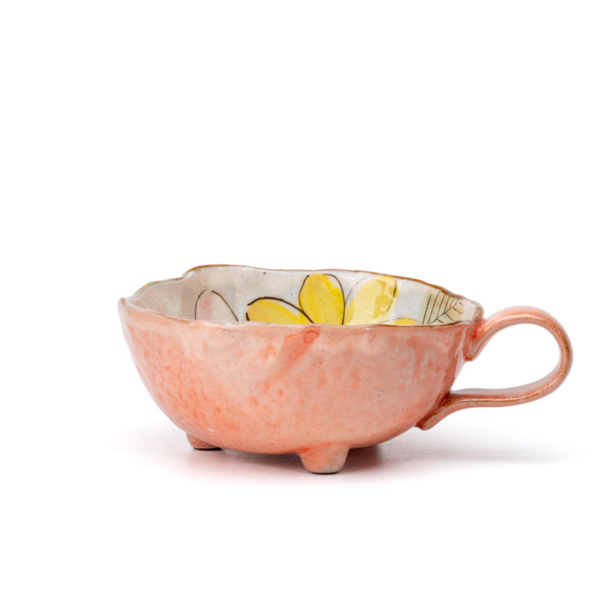 Side view of the orange cup with its rounded handle and three feet.