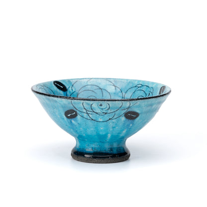 Turquoise footed ceramic dessert bowl with outlined roses and a black base on white.