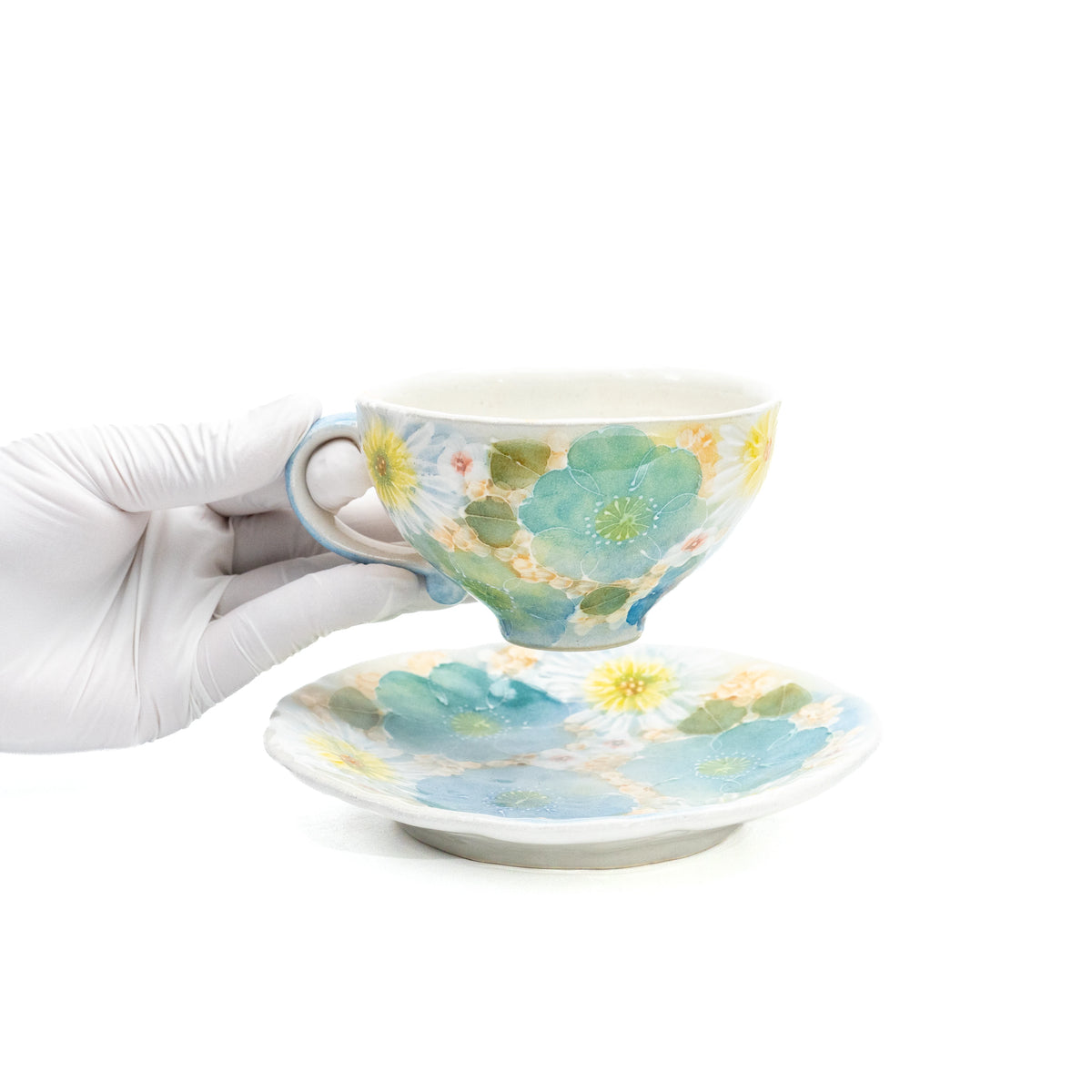 Floral cup held above its matching saucer in a gloved hand.