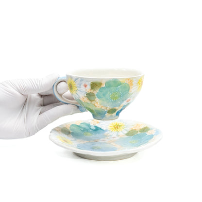 Floral cup held above its matching saucer in a gloved hand.