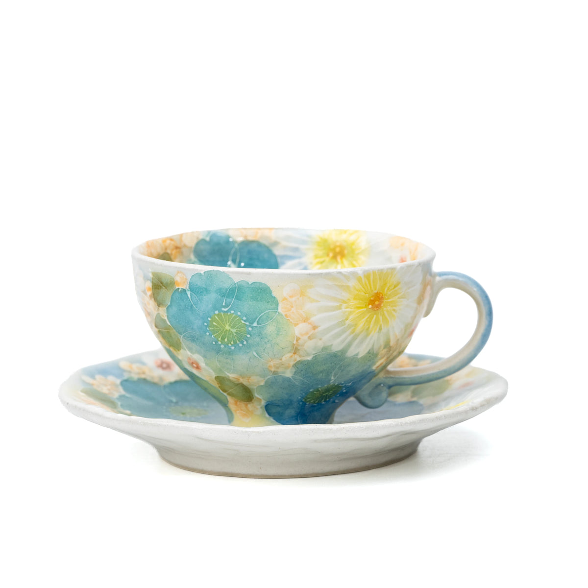Cream porcelain cup and saucer covered with blue, green, yellow and white flowers on white.