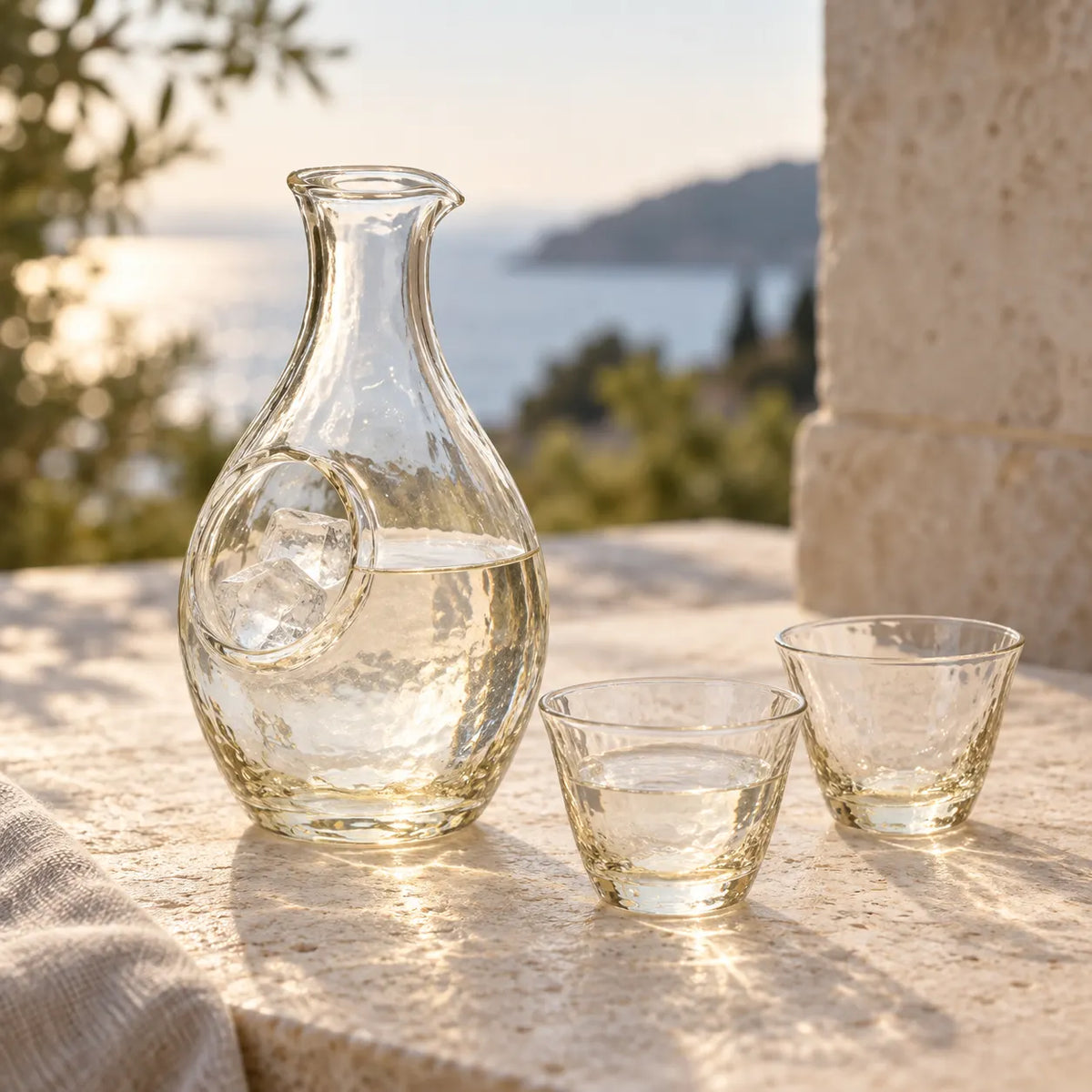 Pale amber glass sake carafe with ice in its separate pocket beside two small matching cups on a stone table