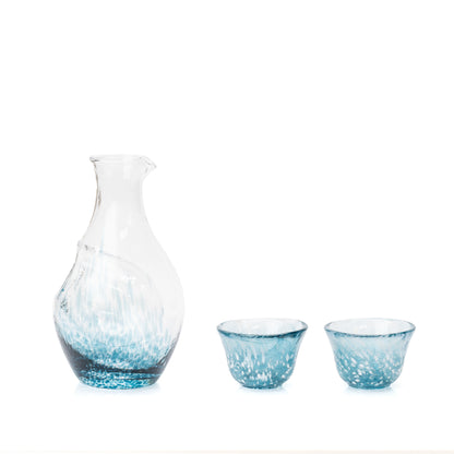 Blue glass sake carafe with an ice pocket and two matching cups on white.