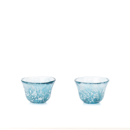Two small blue glass sake cups on white.