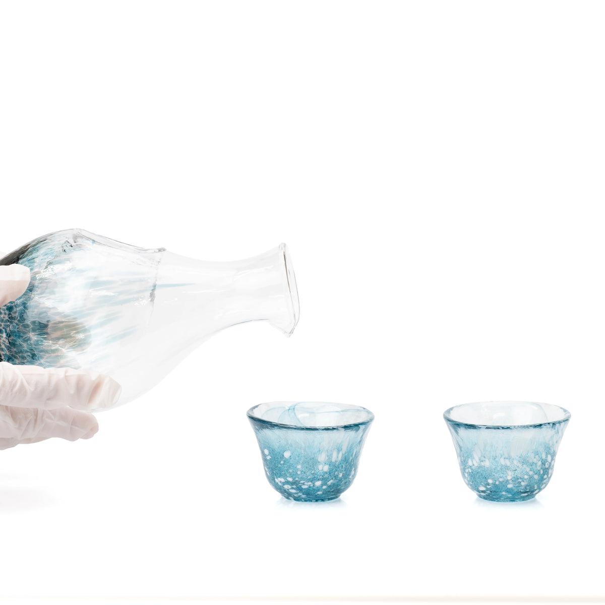 Blue glass sake carafe tilted above the two matching cups.