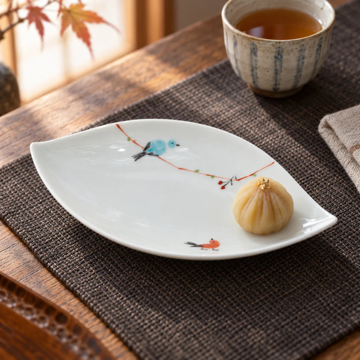 Hasami leaf-shaped porcelain plate with painted blue and orange birds, holding a small sweet beside a cup of tea