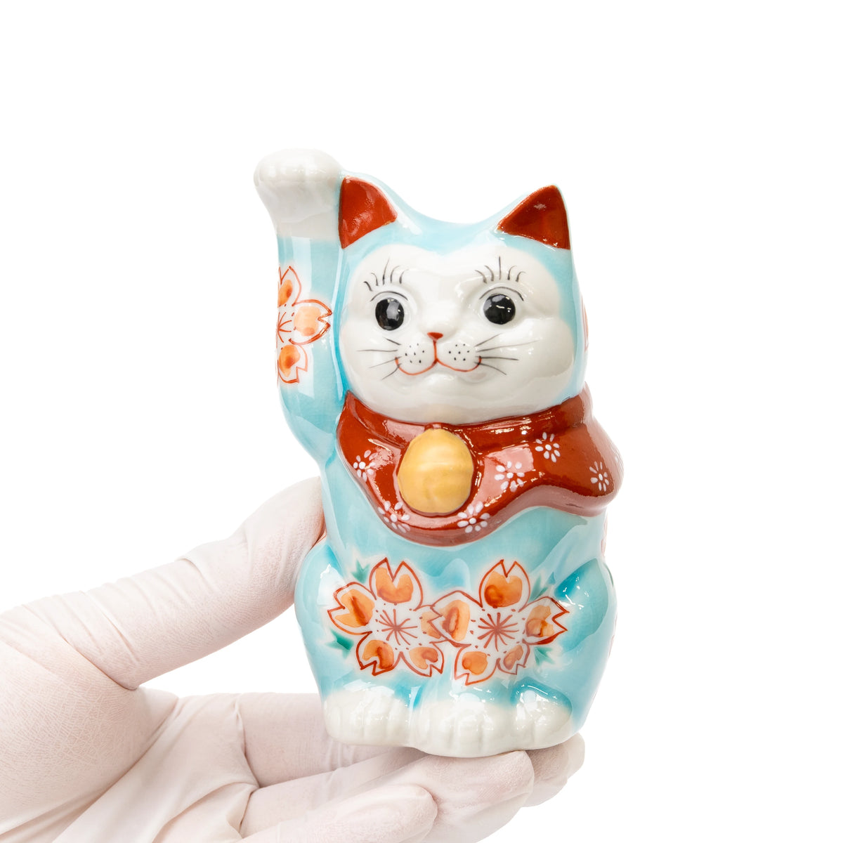 Turquoise cherry blossom lucky cat held in a gloved hand.