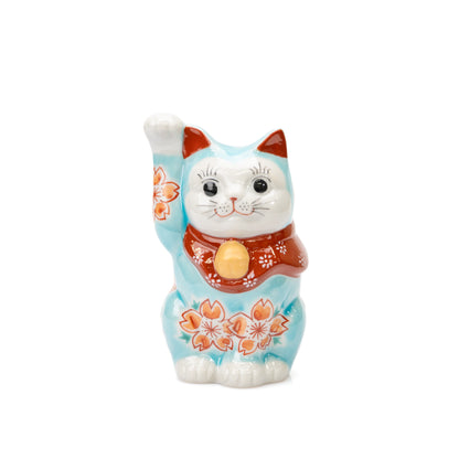 Turquoise Kutani lucky cat with raised right paw, cherry blossoms and a red bib on white.