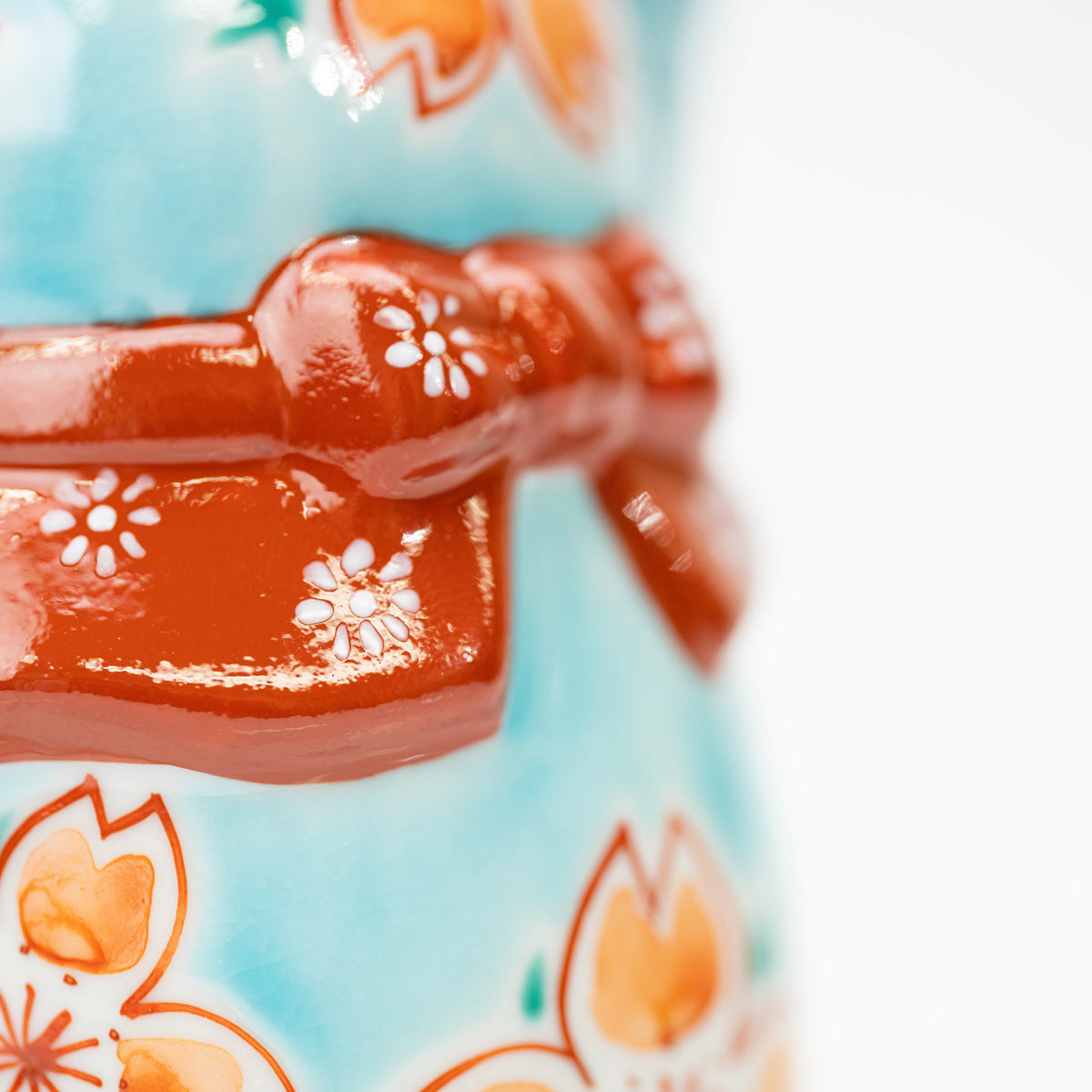 Red bow across the turquoise lucky cat's back.
