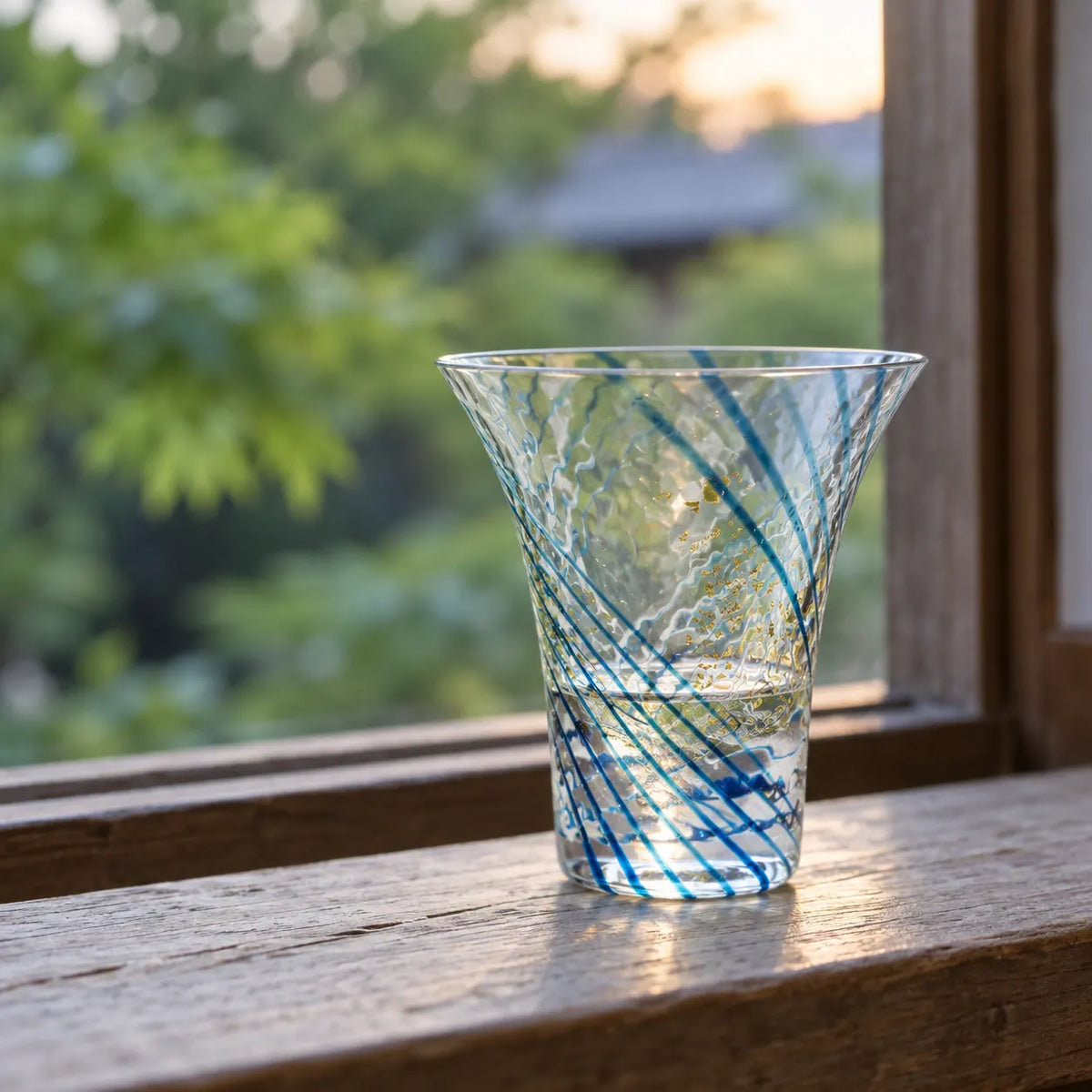 Single flared blue and gold leaf sake cup with a little clear sake on a wooden windowsill