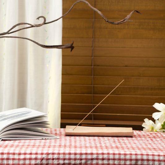 Brown floral incense holder on a red checked tablecloth beside a book and white flowers.