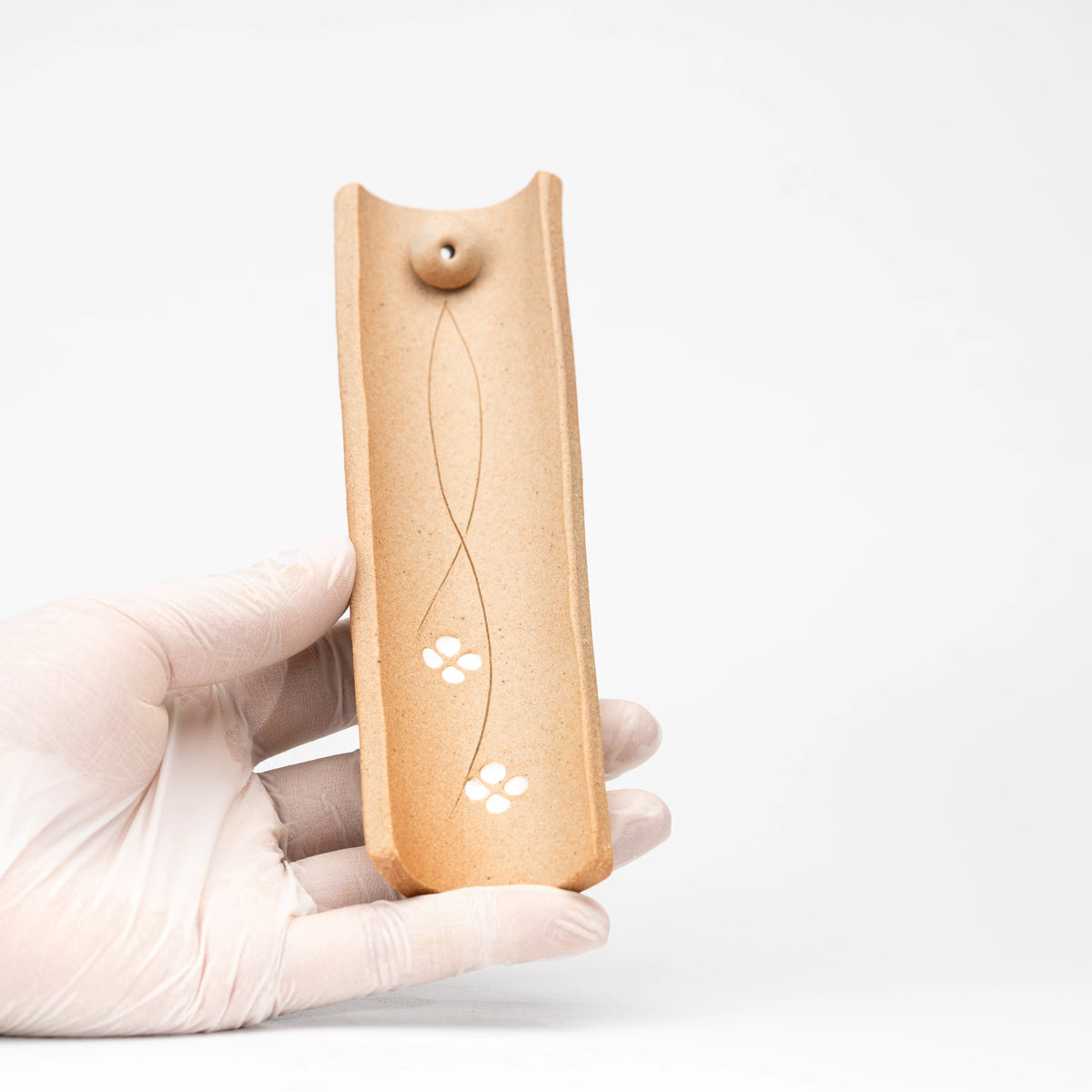 Brown floral incense holder held vertically in a gloved hand.