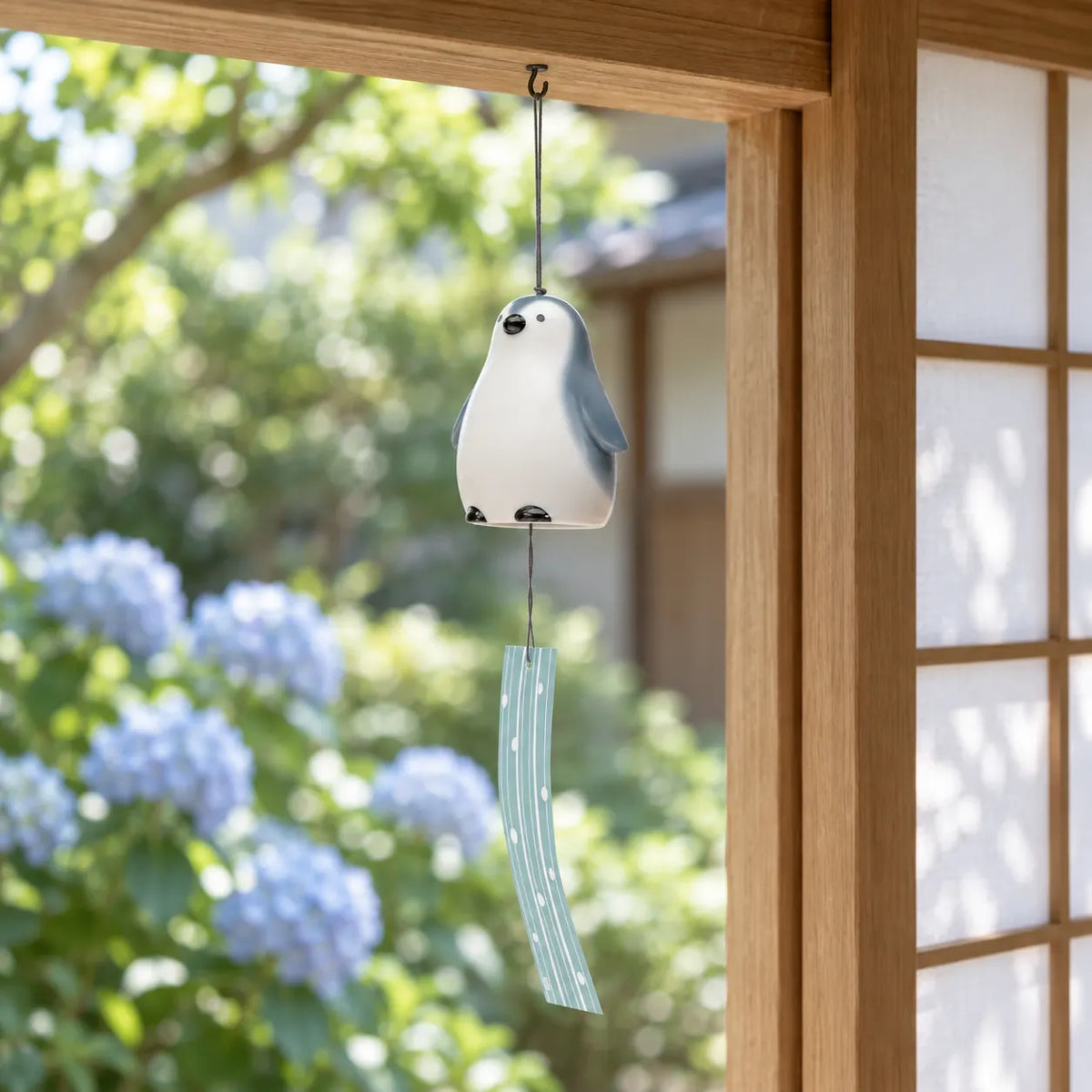 Yakushigama porcelain penguin wind chime with pale blue striped paper hanging by summer hydrangeas