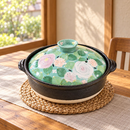 Yuzuriha Green Rose donabe with a hand-painted green floral lid on a woven trivet by a sunlit window.