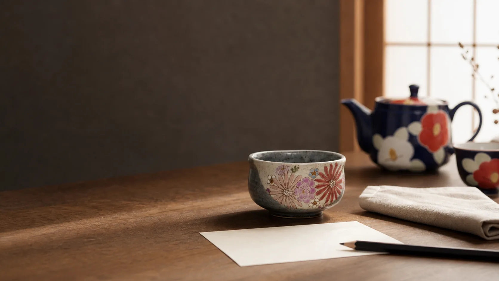 A Japanese teacup beside a blank note card and pencil on a quiet wooden desk.